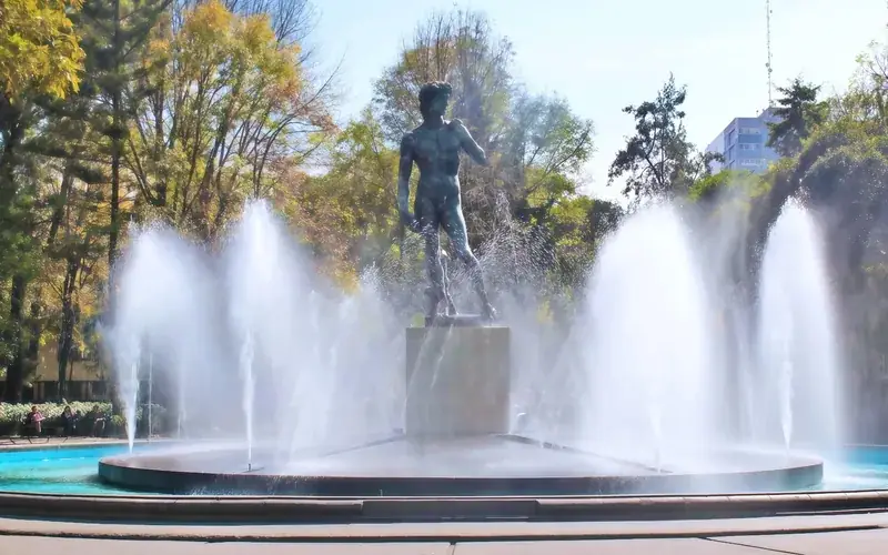 Fuente escultórica rodeada de árboles en la Colonia Roma Norte, Ciudad de México.